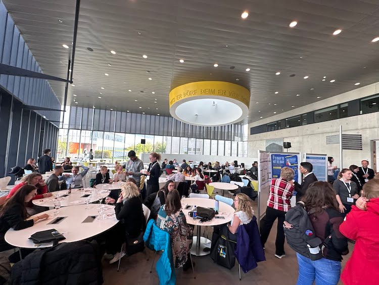 photo of people mingling in a large, open room with poster displays and tables for seating