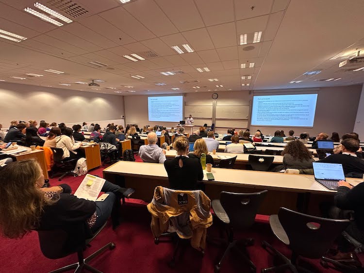 Several dozen people in a stadium-seating classroom watching a keynote presentation with slide deck